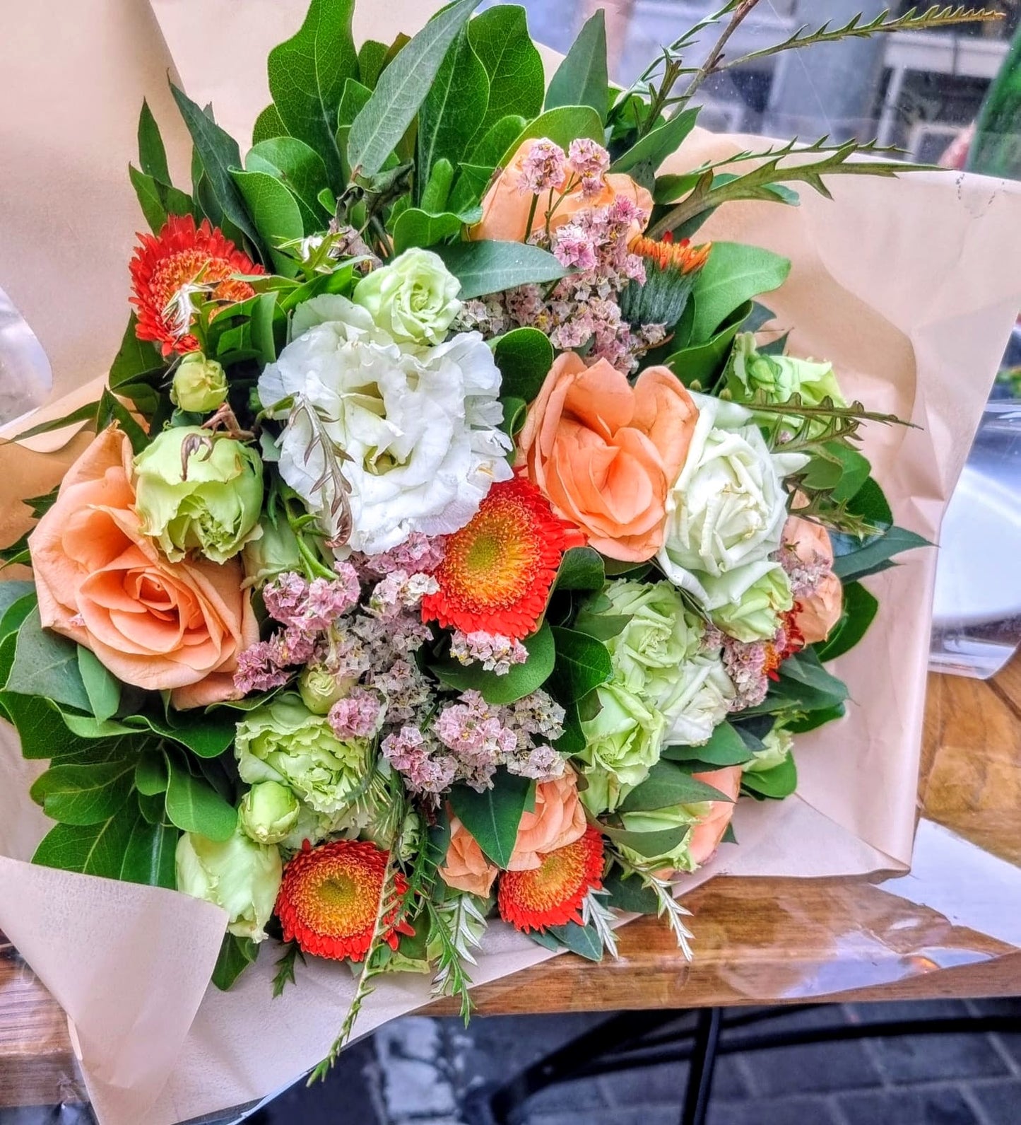 Bouquet of flowers with green, orange, and white colors on a wooden table.