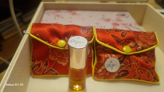 Small bottle of perfume with two red fabric pouches on a white surface