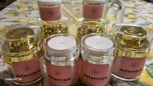 Multiple jars of 'Artemisia' brand cream, with clear glass jars and gold-colored lids, displayed on a surface. The product label is visible on the jars, indicating the brand name and possibly the floral theme.