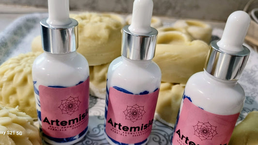 Three bottles of Artemis skincare product with pink labels on a textured surface.