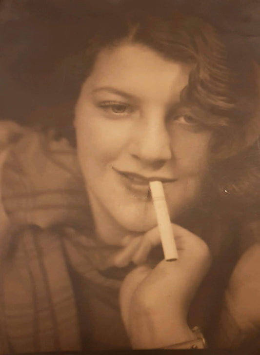 A person holding a cigarette to their mouth, with a blurred background. Tante Trude